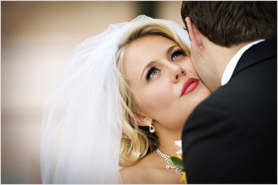 beautiful bride is kissed on the cheek by her husband