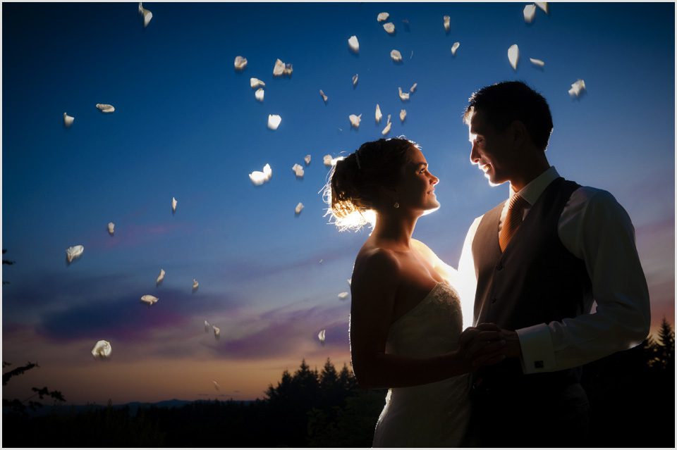 groom looks at bride while petals fall through the air